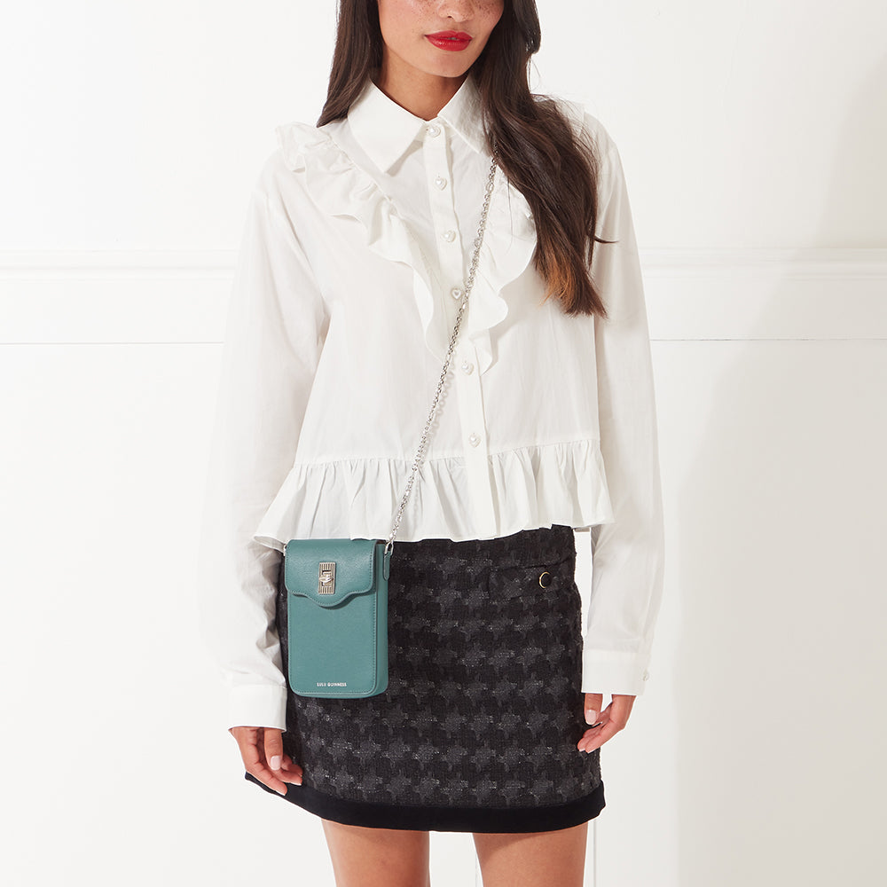 Woman in white ruffled blouse and black and white houndstooth skirt with teal crossbody phone bag.
