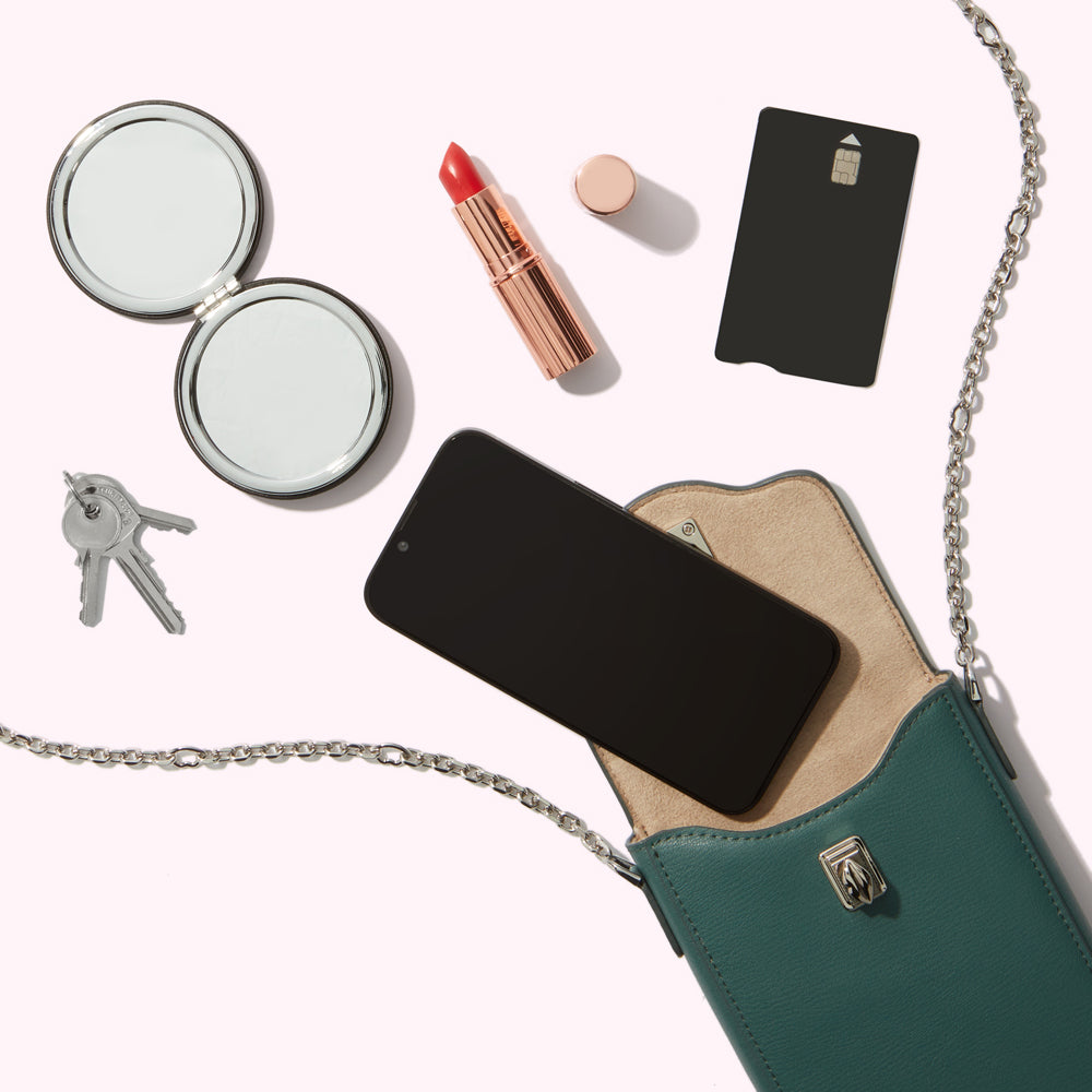 Contents of a teal crossbody bag on a white background: keys, a compact mirror, lipstick, a credit card, and a smartphone.