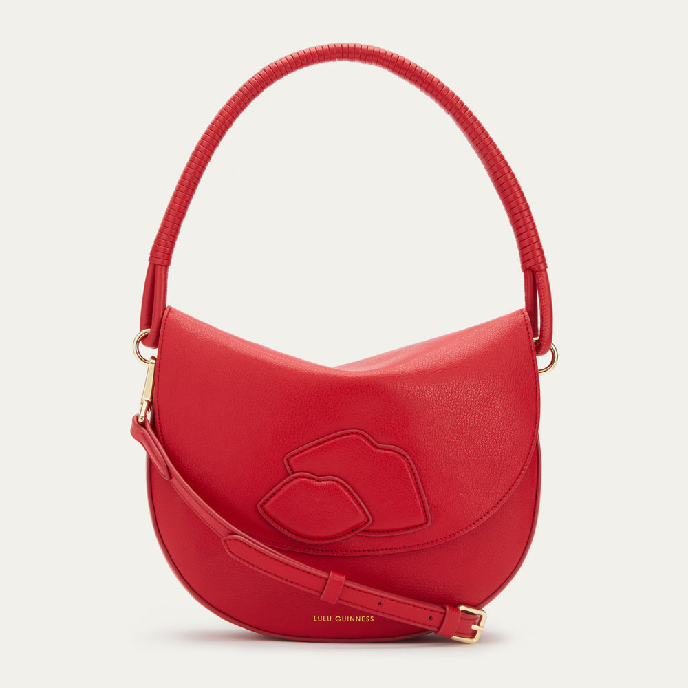 Red Lulu Guinness crescent-shaped handbag with lips detail on a beige background.