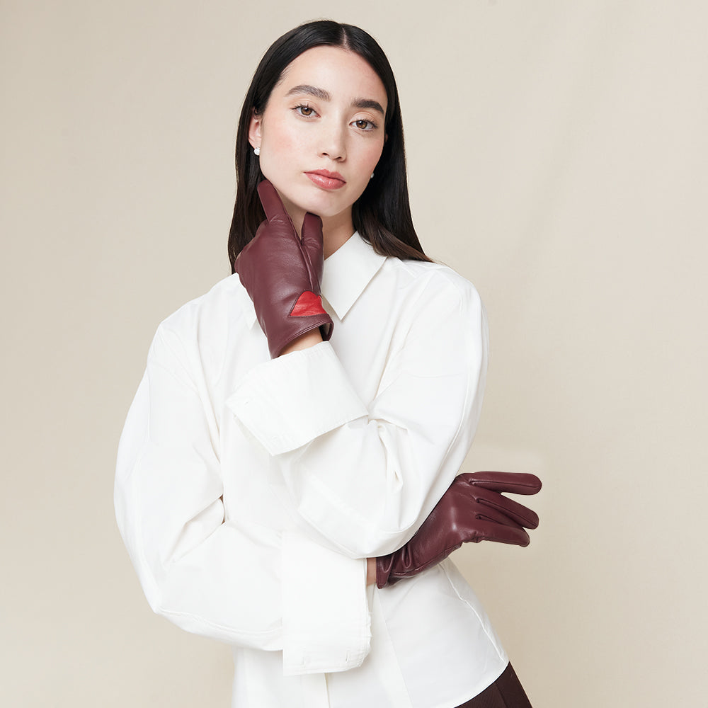 Woman wearing a white shirt and burgundy leather gloves against a beige background