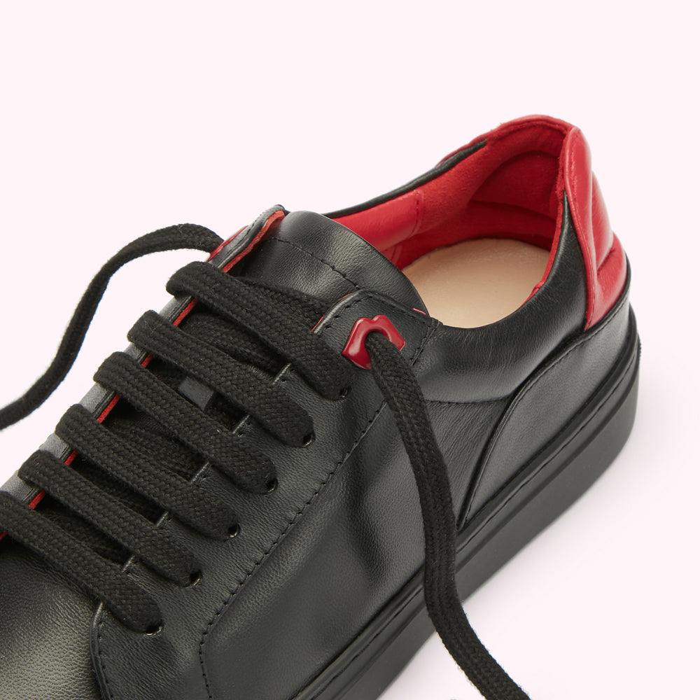 Close-up of black leather sneaker with red inner lining and laces.
