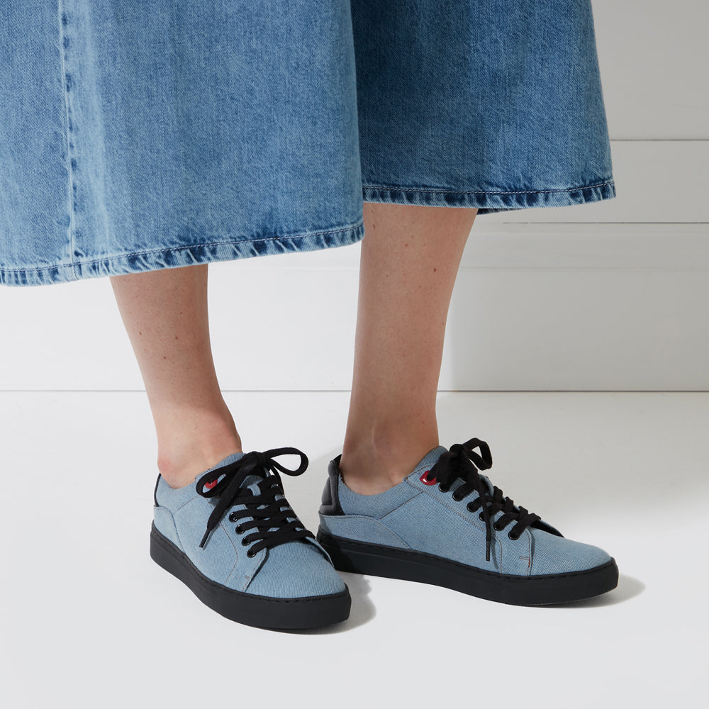 A person wearing light blue denim sneakers and a denim skirt against a white background.
