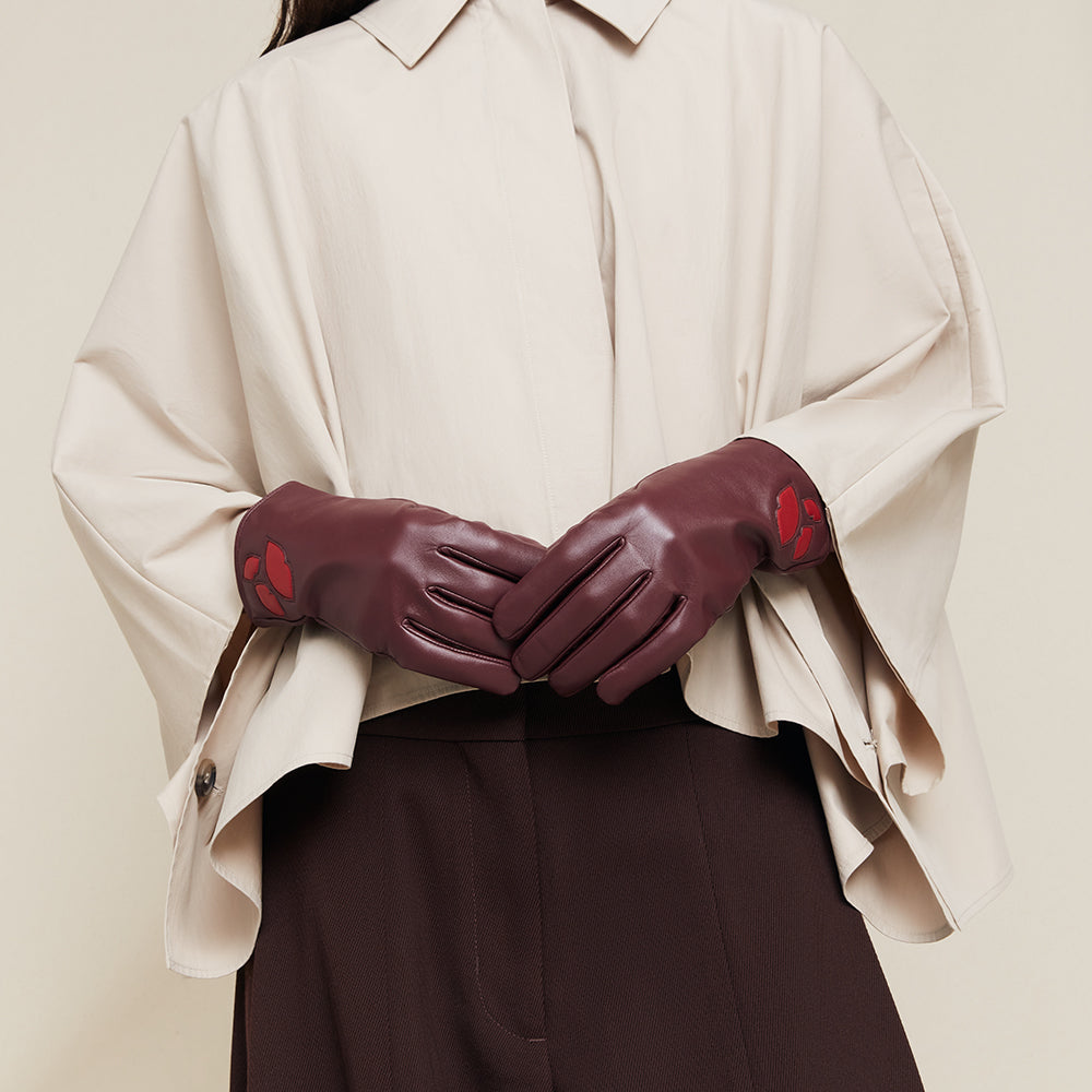 Person wearing burgundy leather gloves with lip details on a beige background