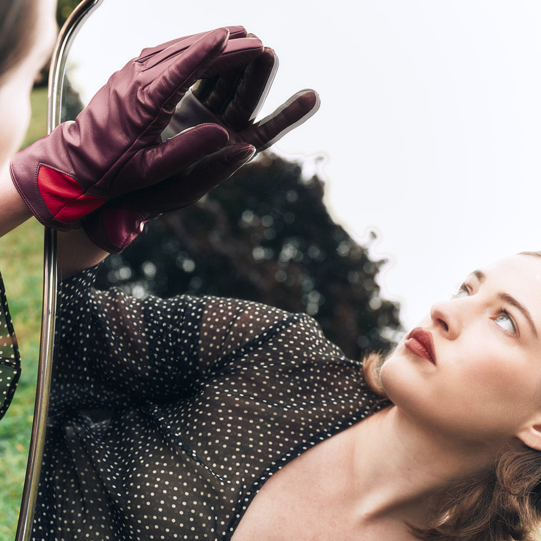 Person wearing a burgundy glove and polka dot dress in front of a mirror