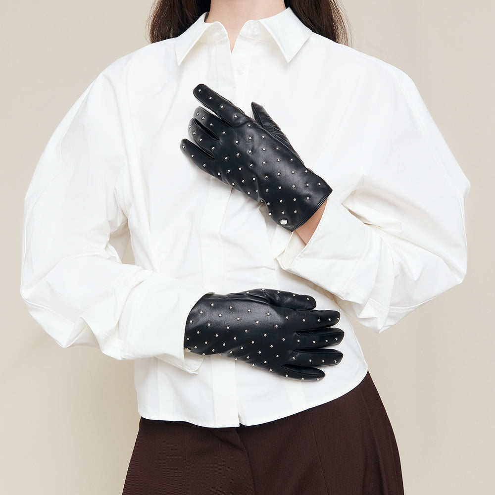 Person wearing black leather gloves with studs and a white shirt on a beige background