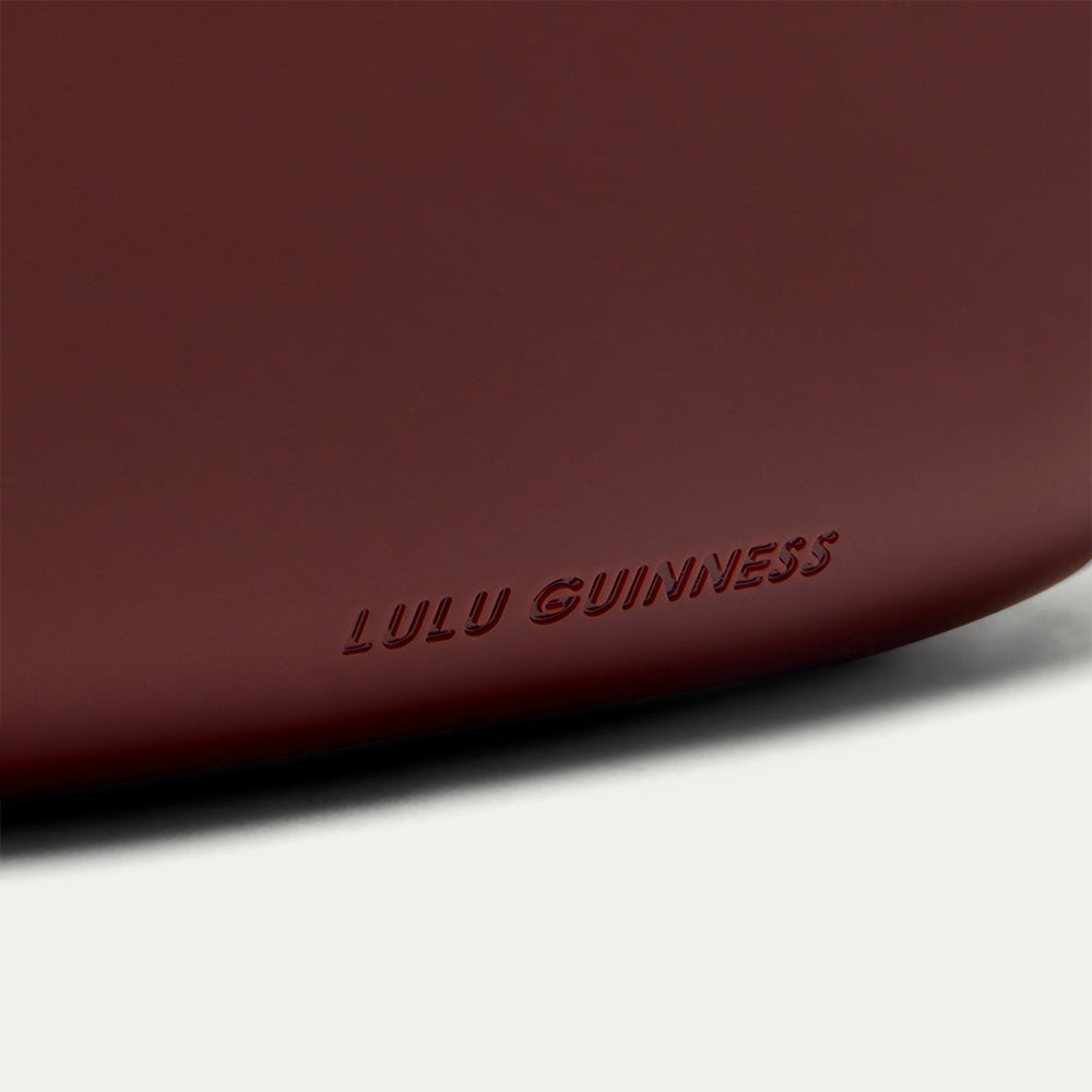 Close-up of a burgundy clutch bag with 'Lulu Guinness' branding on a white background
