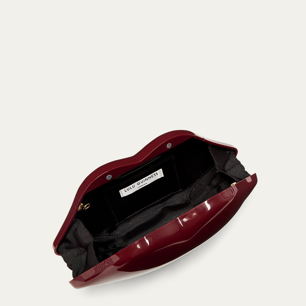 Burgundy red lip-shaped handbag open revealing a black lining and a 'Lulu Guinness' label on a white background