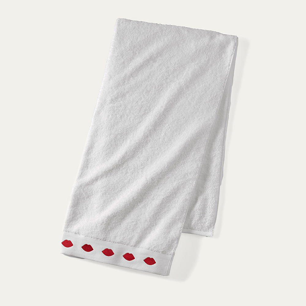 A white bath towel folded with red lips along the edge on a beige background