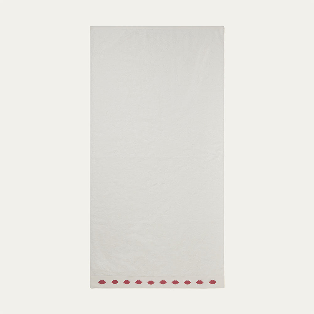 A white bath towel flat with a row of red lips on the edge on a beige background