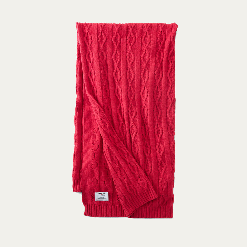 A red lip cable knit throw folded on a beige background
