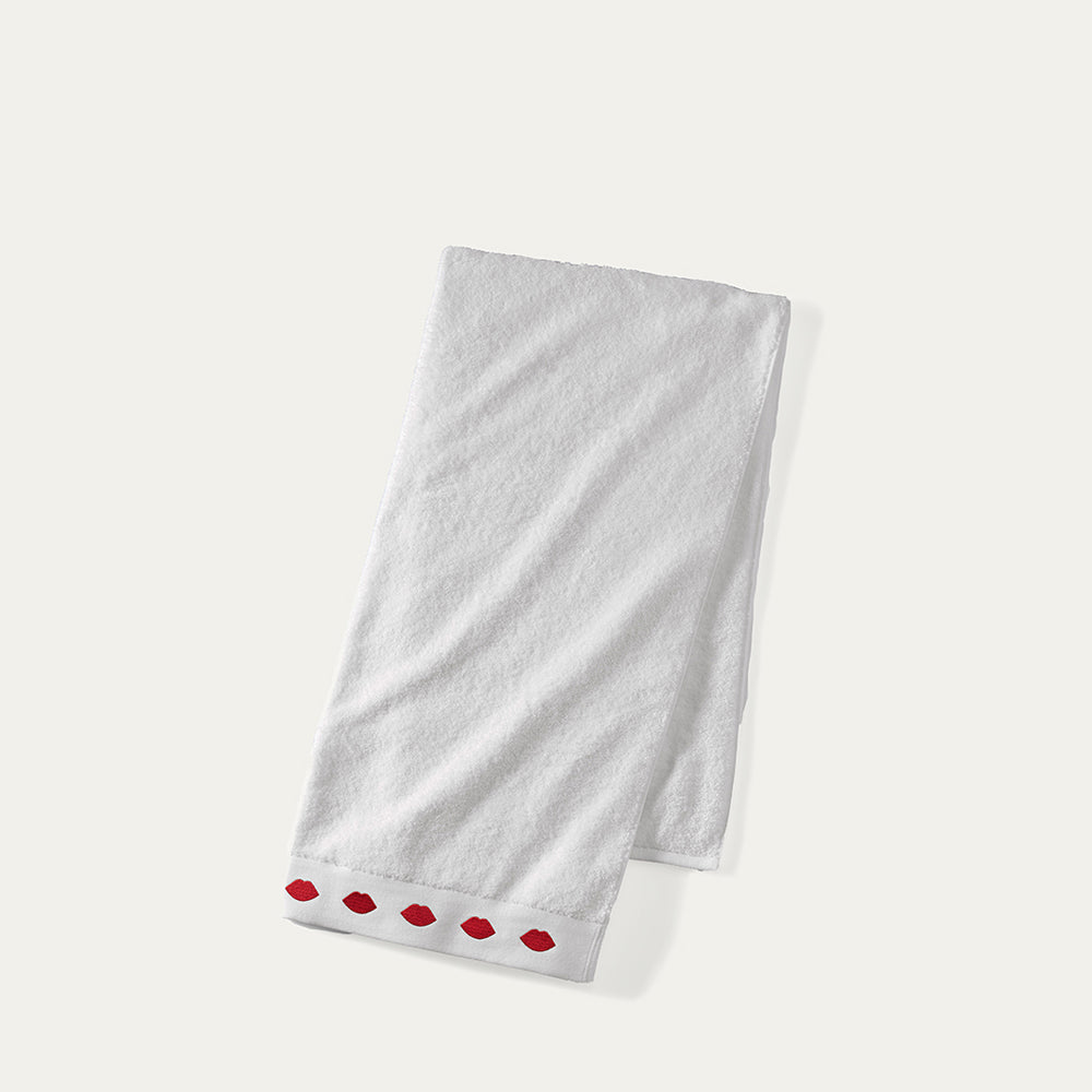 A folded white hand towel with a row of red lips on the edge on a beige background