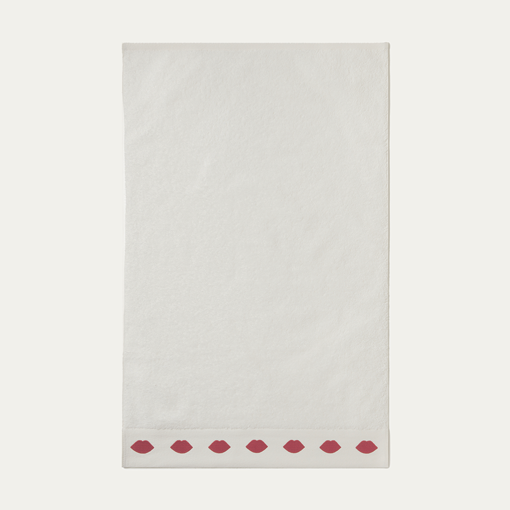 A white hand towel with a row of red lips on the edge on a beige background
