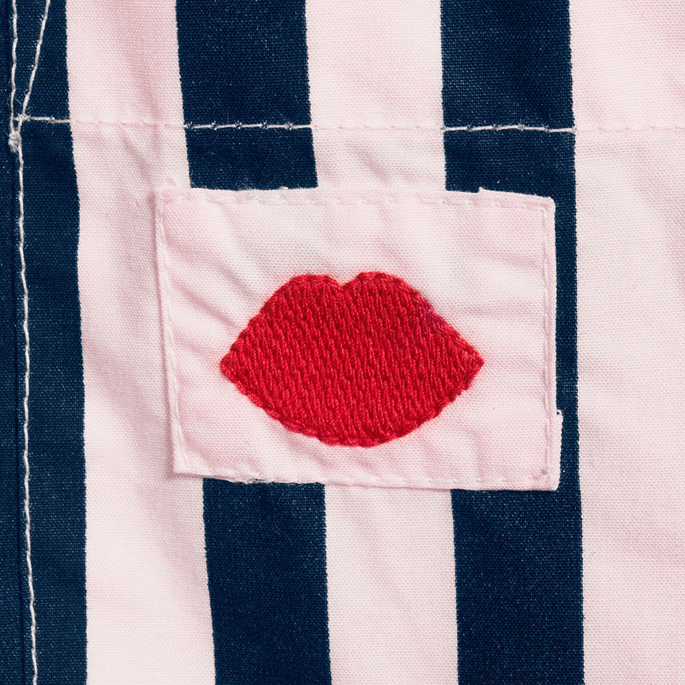 Close-up of a red embroidered lip on a navy and pale pink striped pyjama shirt.