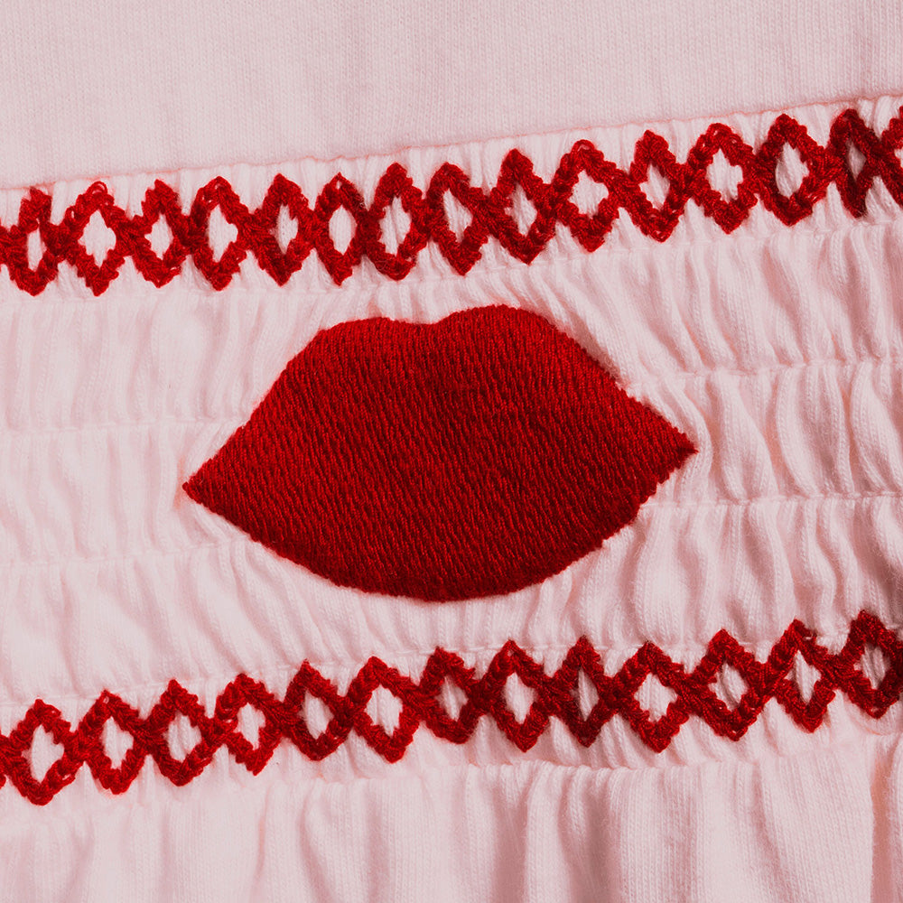 Close up of red embroidered lips on a pink pyjama shirt.