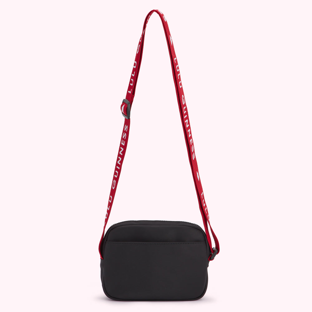 Black crossbody bag with a red adjustable strap that has the words "LULU GUINNESS" printed on it.