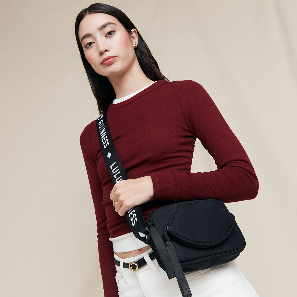 Woman holding a black crossbody bag with visible 'Lulu Guinness' against a beige background