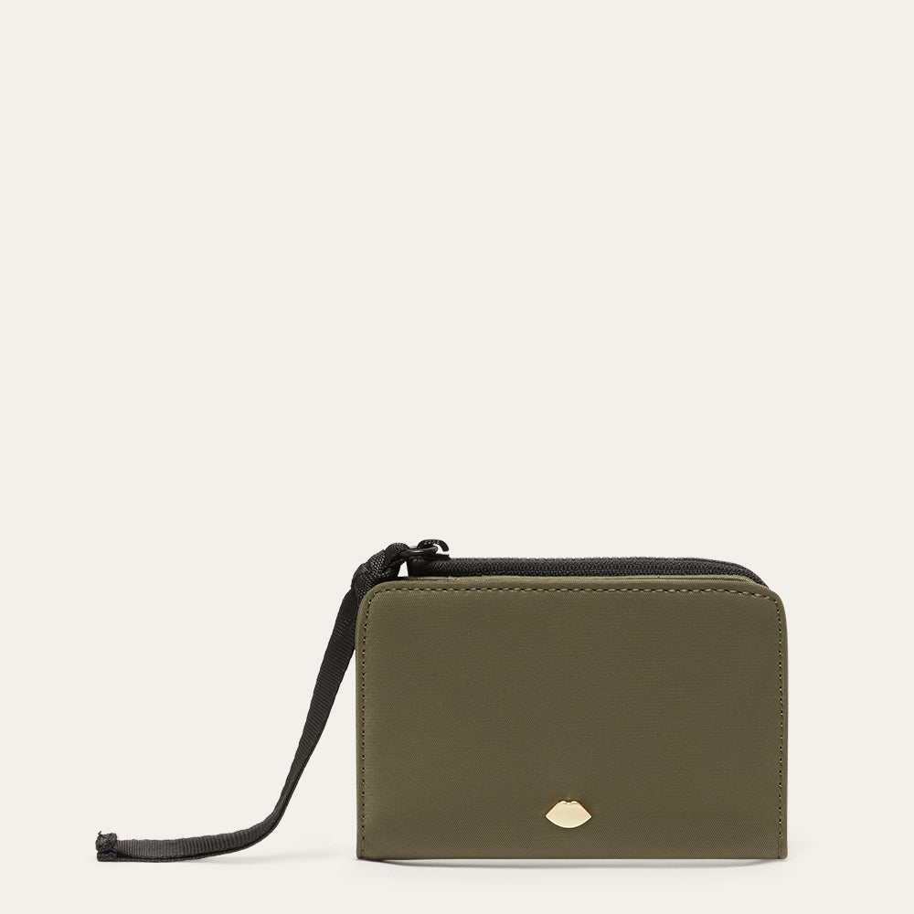 Green wallet with a gold metal  lip stud and black ribbon zip pull on a light beige background