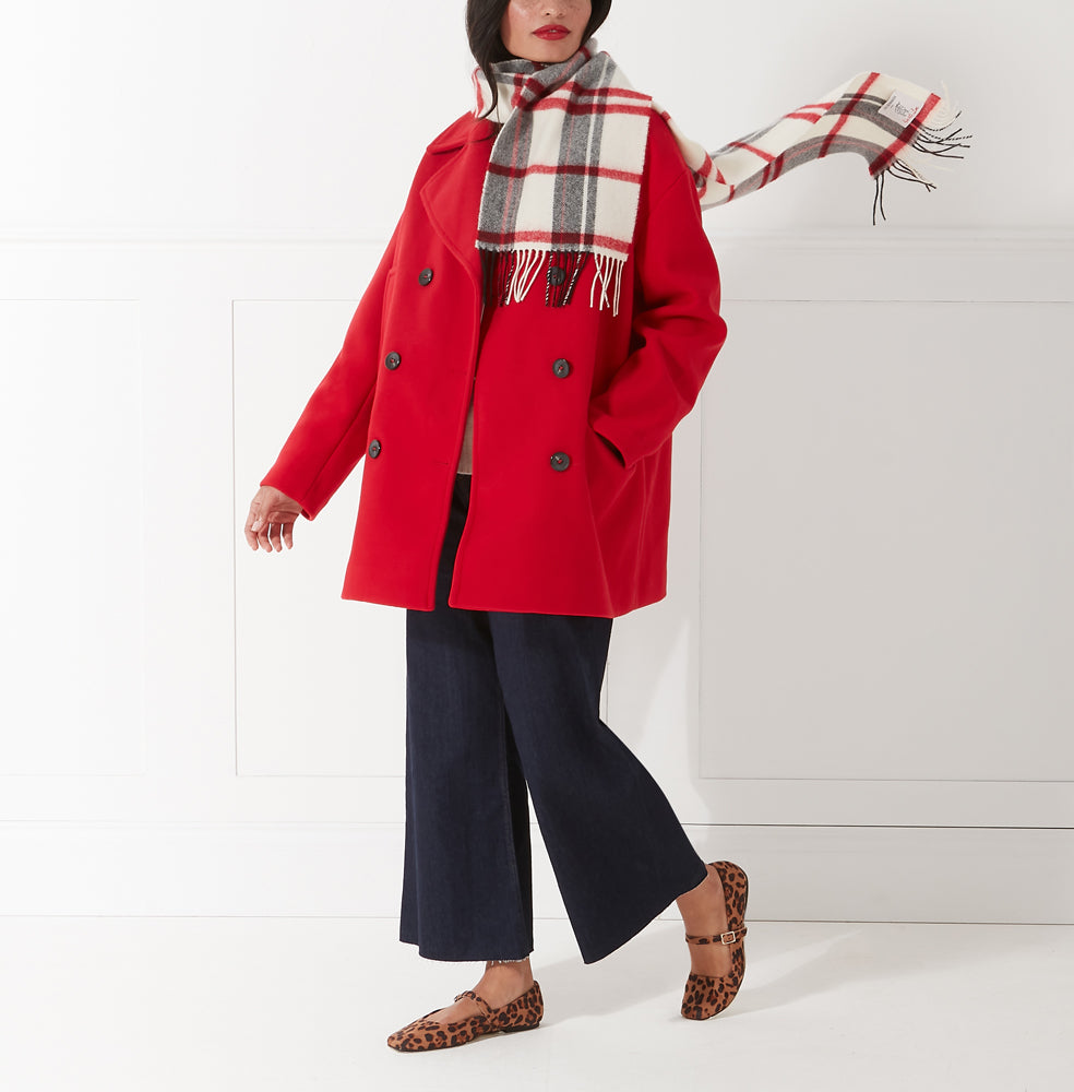 Woman in red coat, cream and red plaid or tartan scarf, dark blue pants, and leopard print flats against a white background.
