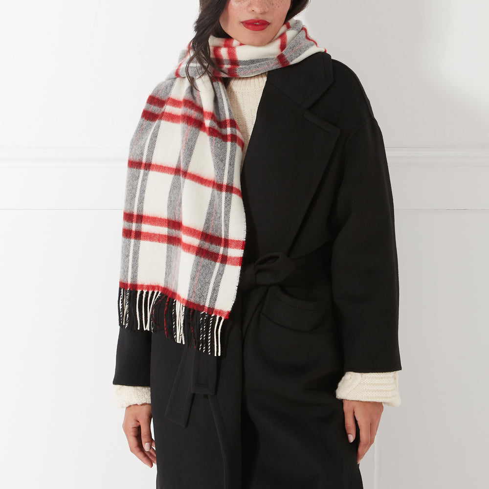 Woman wearing a black coat and a red and grey plaid or tartan scarf against a white background.