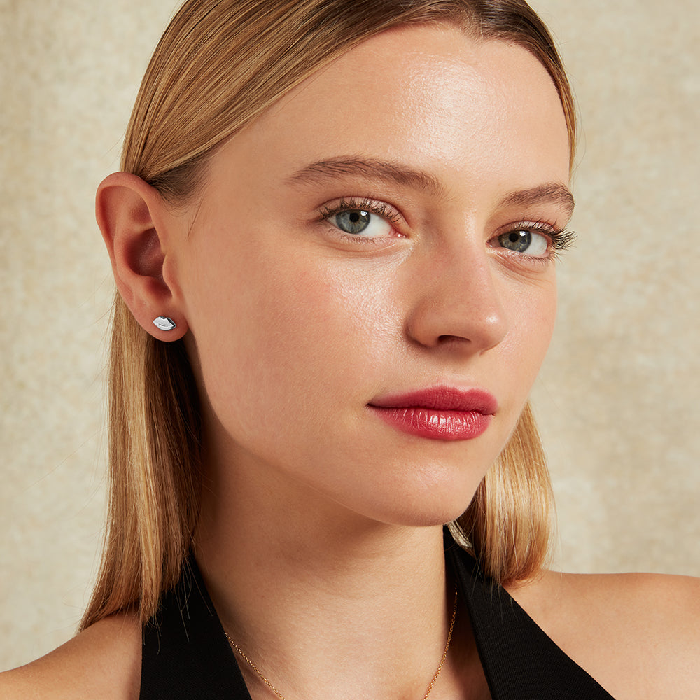 Close-up of a woman's face wearing a silver lip-shaped stud earring with a neutral background