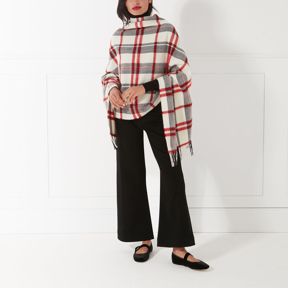 Woman wearing a red and white plaid or tartan poncho, black pants, and black shoes against a white background.