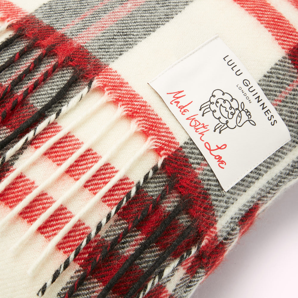 Close-up of a cream, red, and black plaid or tartan Lulu Guinness scarf with fringe and a label that reads "Made with Love."