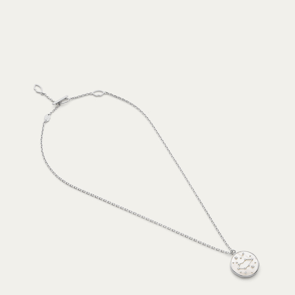 Silver necklace with a round pendant with a star and constellation design on a light gray background