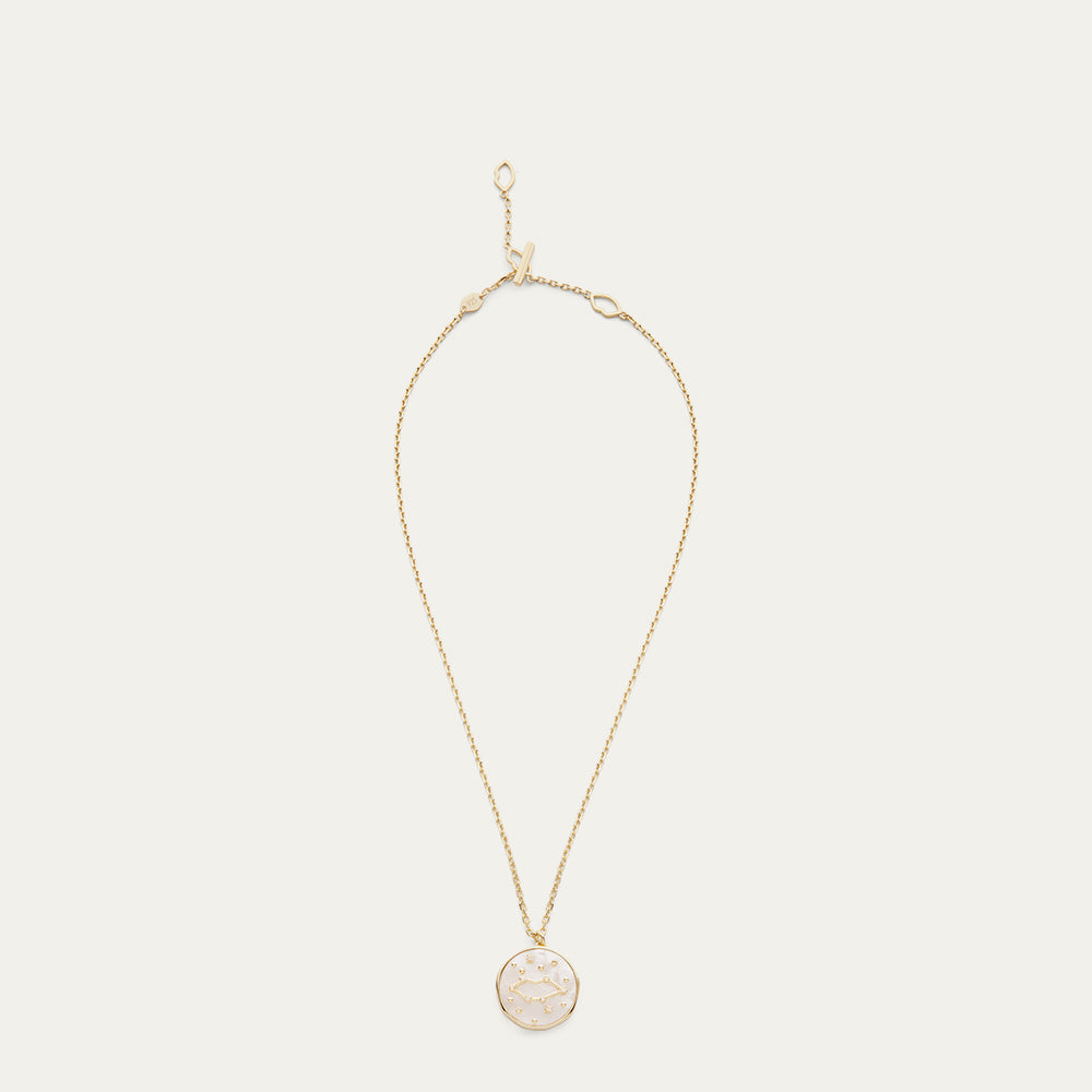 Gold necklace with a round pendant with a star and constellation design on a light beige background