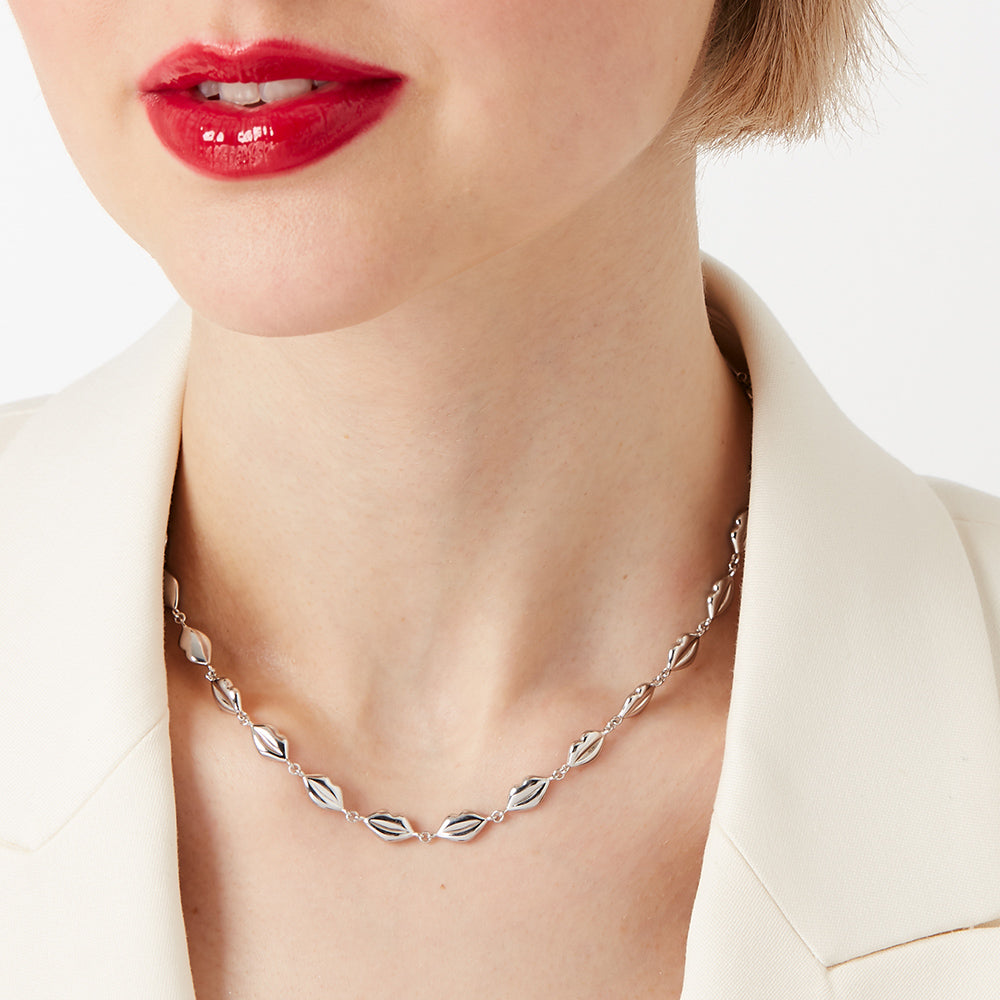 Close-up of a woman wearing a silver necklace with lip-shaped charms against a white background.