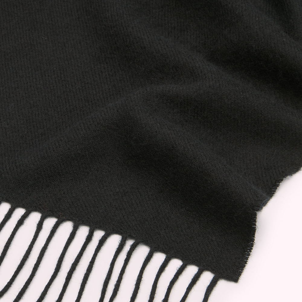 Close-up of a black fringed scarf against a white background.
