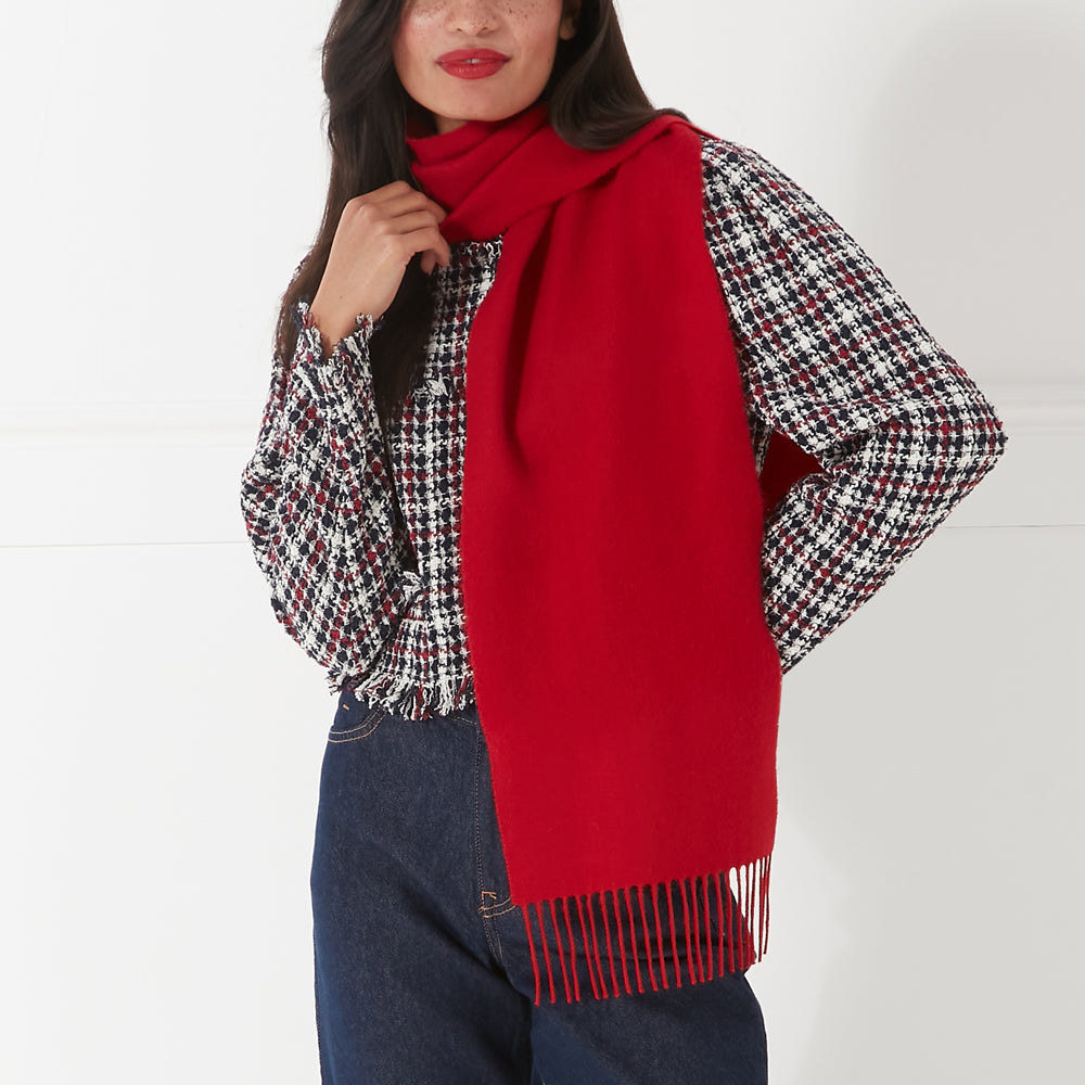 A woman wearing a red fringed scarf against a white background.