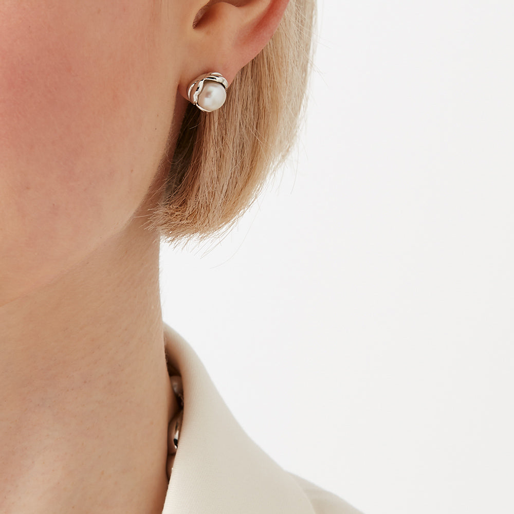 Close-up of a person's ear wearing a pearl stud earring against a white background.
