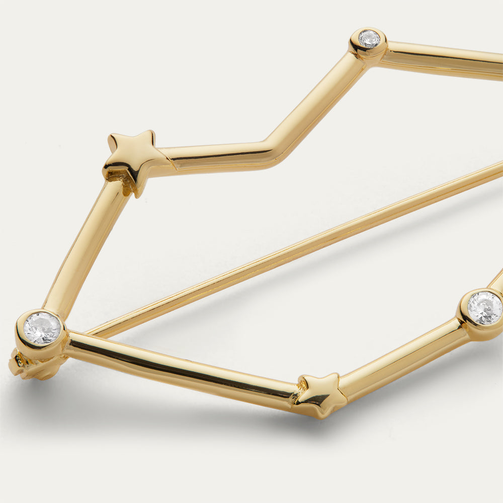 Close up image if a gold lip shaped constellation brooch with star design and crystal details on a white background