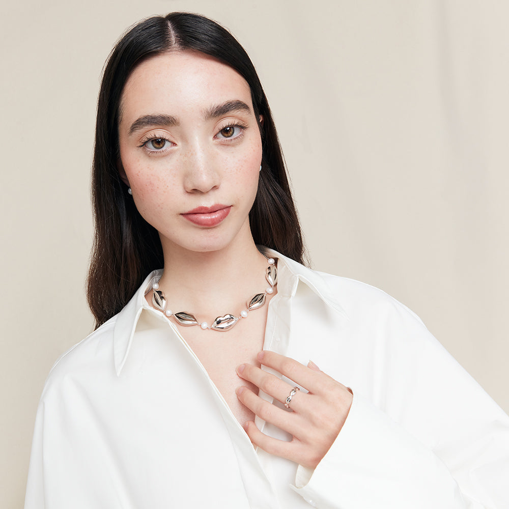 Woman wearing a silver lip and pearl necklace with a plain background