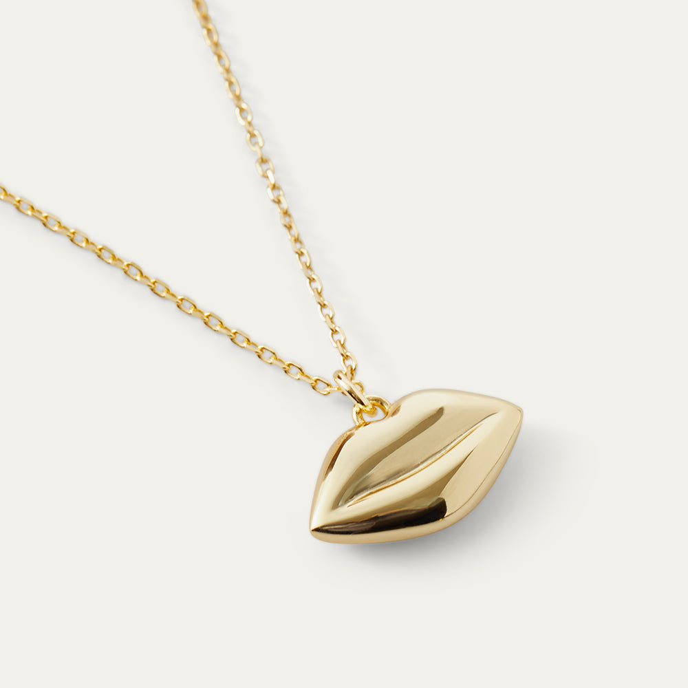 Gold necklace with a lip-shaped pendant on a light gray background