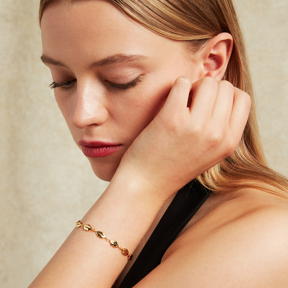 Woman wearing a gold lip link bracelet and touching her ear, with a neutral background
