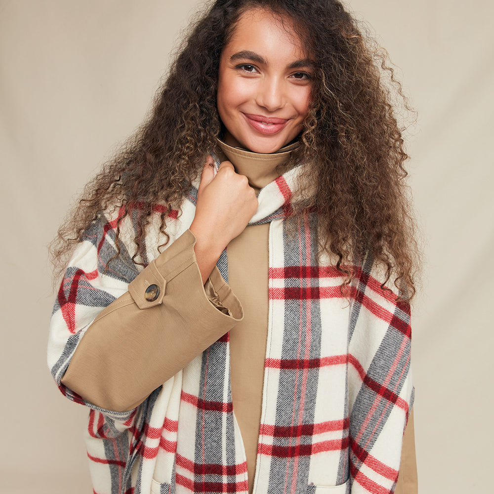 Woman wearing a beige coat with a plaid jacket against a beige background