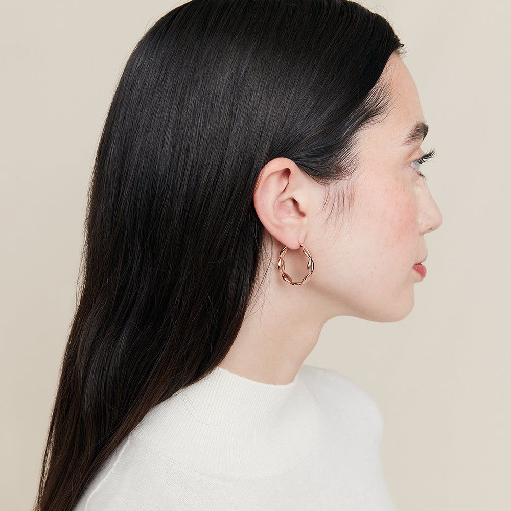 Woman wearing a rose gold hoop earring against a beige background