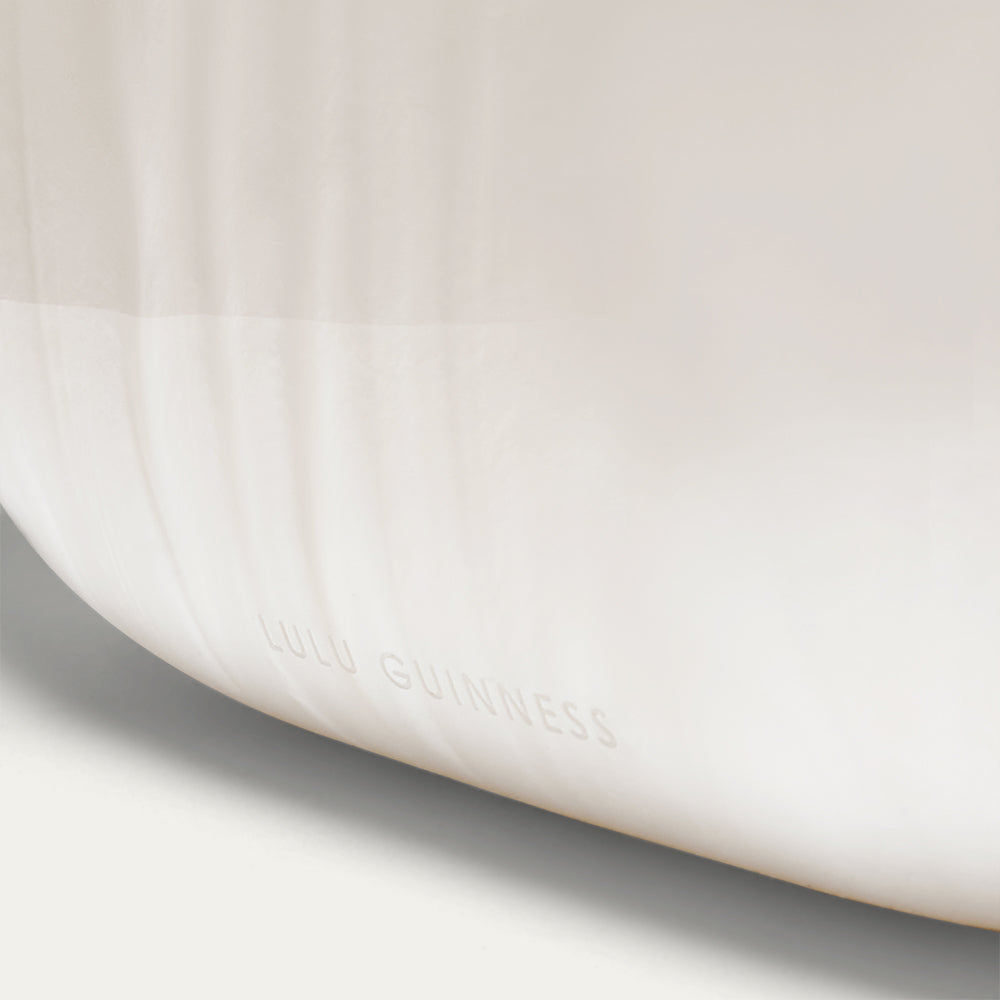 Close-up of a white clutch with 'LULU GUINNESS' branding on a light gray background