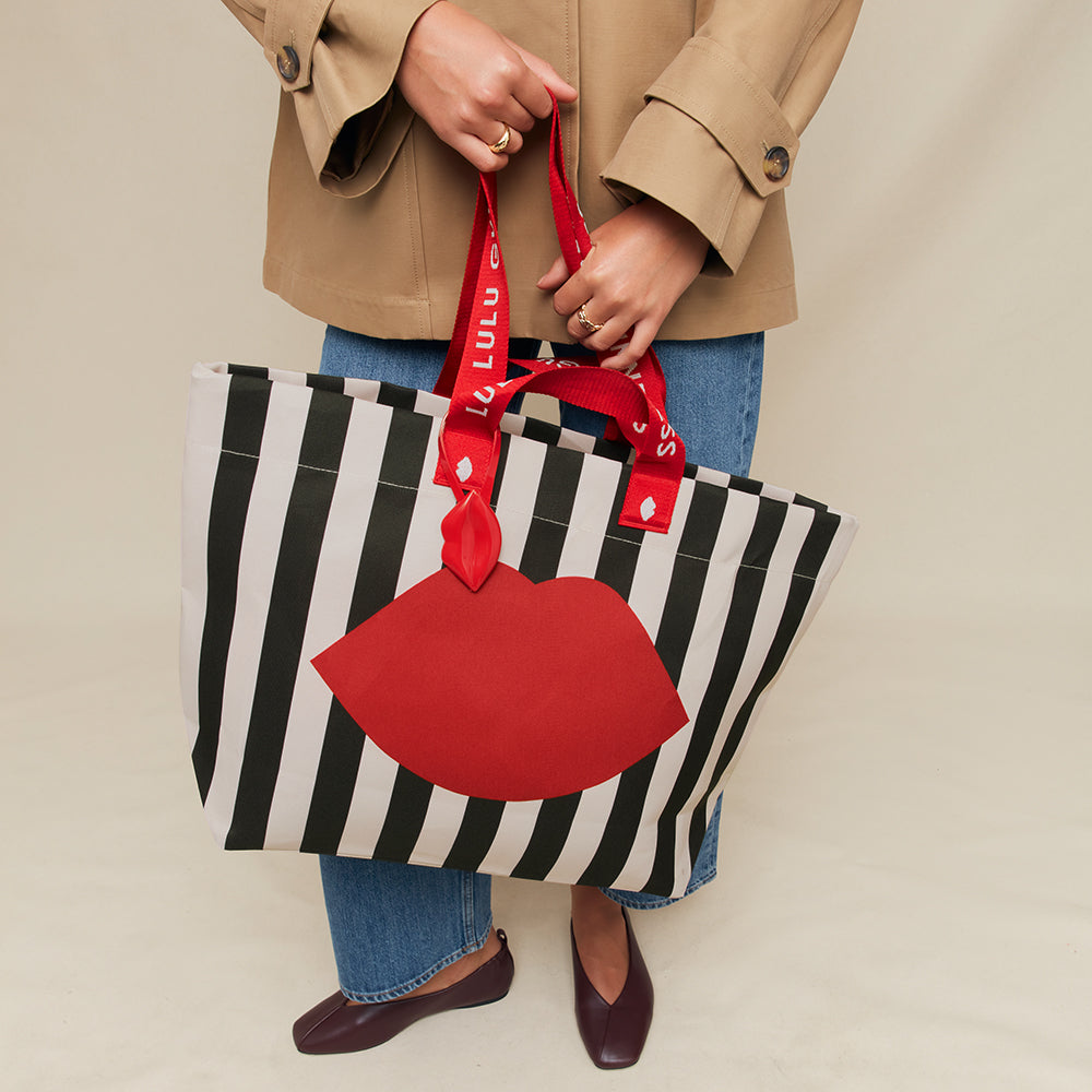 Person holding a black and white striped tote bag with a red lip design and a matching red bag.