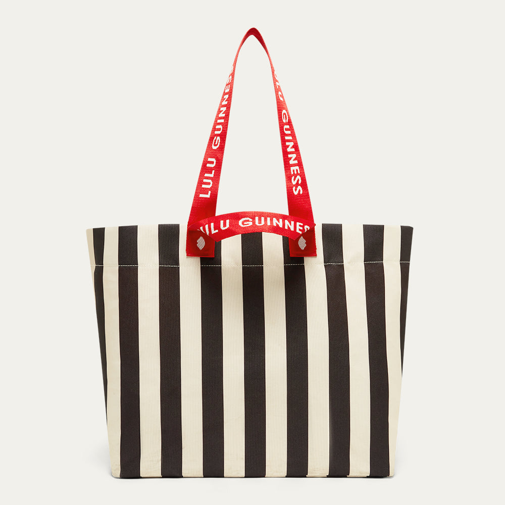 Black and beige striped tote bag with red handle featuring 'Lulu Guinness' branding on a light gray background.