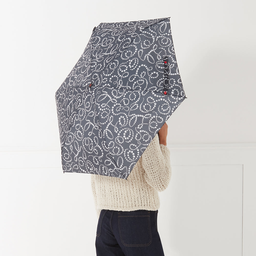 A person holds a dark gray umbrella with a white pearl pattern behind their back against a white background.