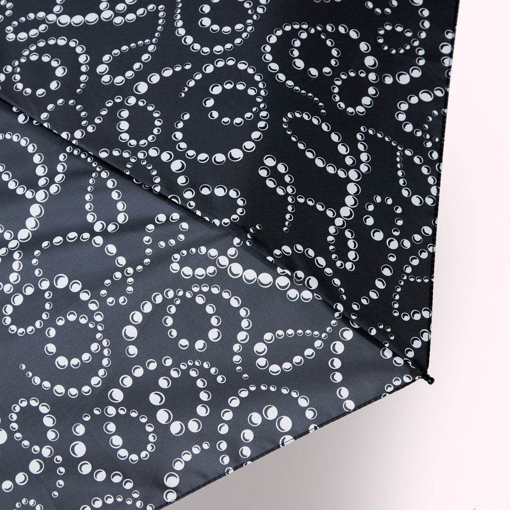 Close-up of a dark gray umbrella with a pattern of white pearl-like circles arranged in swirling designs.