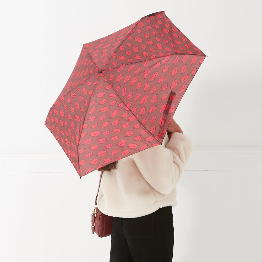 Woman holding a compact red umbrella with a lipstick print against a white background.