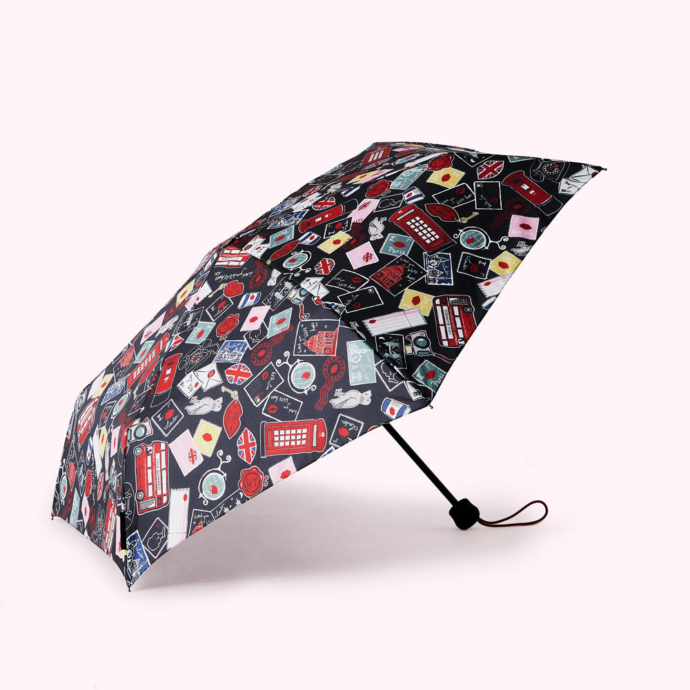 Compact travel umbrella with a dark background and a colorful pattern featuring London landmarks, postmarks, and other travel-themed imagery.
