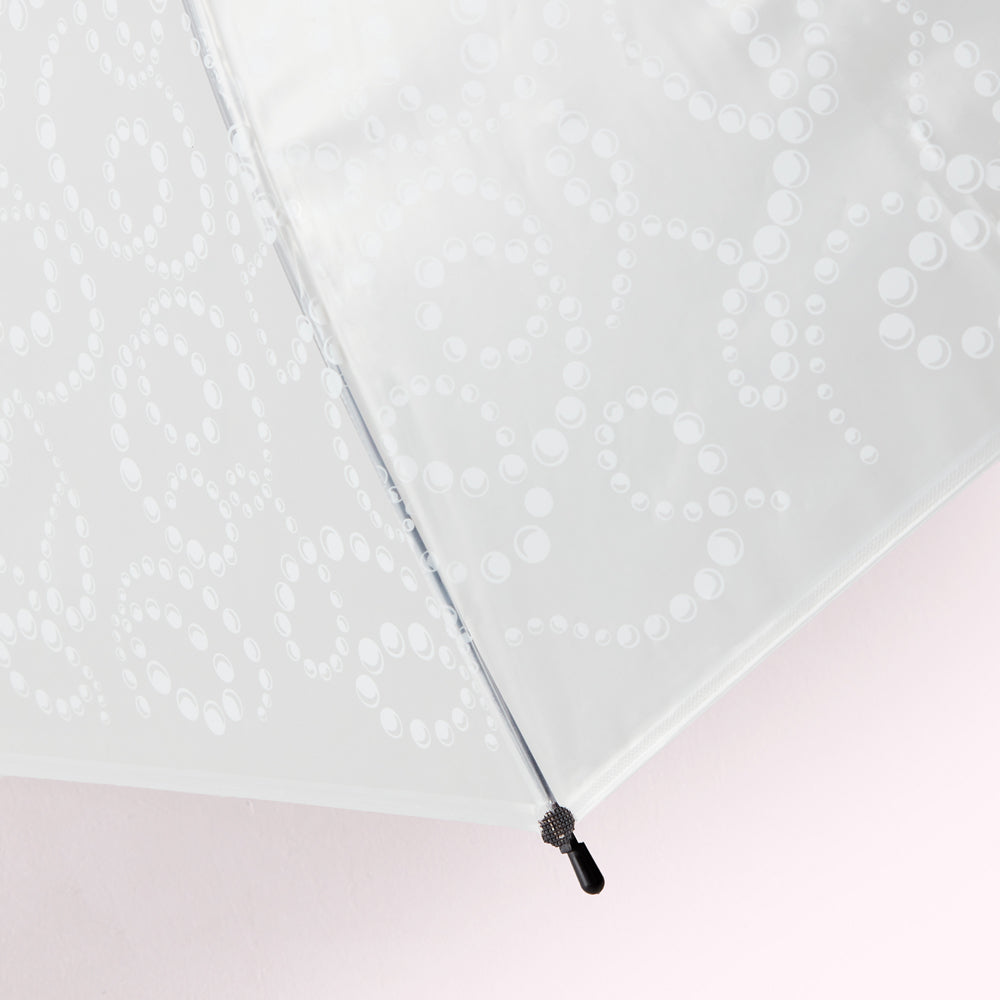 Close-up of a white umbrella with a pearl pattern on a light pink background.