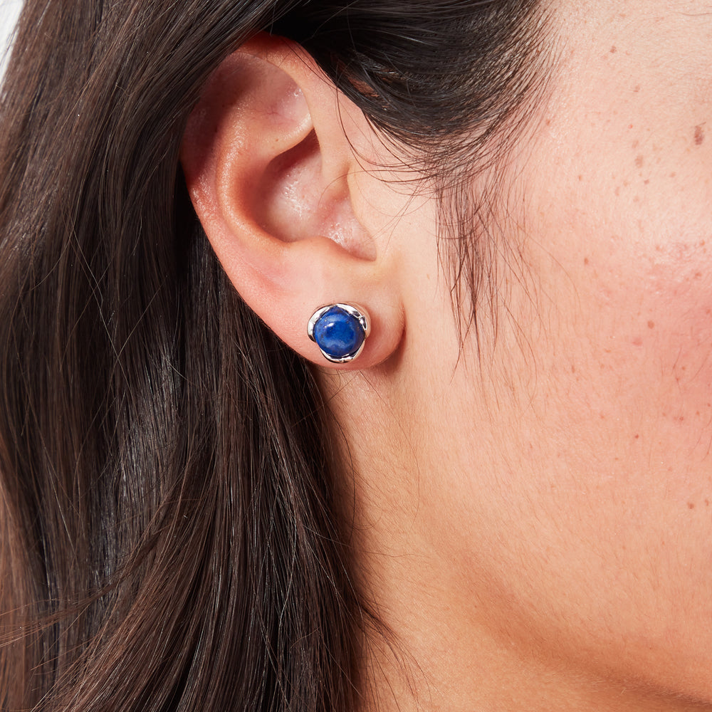 Close-up of a person's ear wearing a lapis lazuli stud earring with a silver setting.
