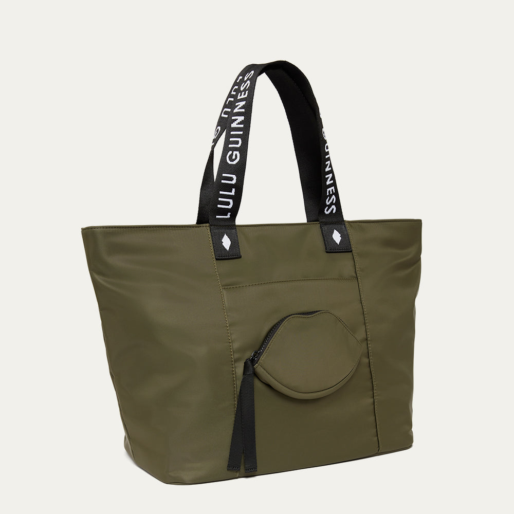 Green tote bag with black handles and a lip-shaped pocket on the front on a white background