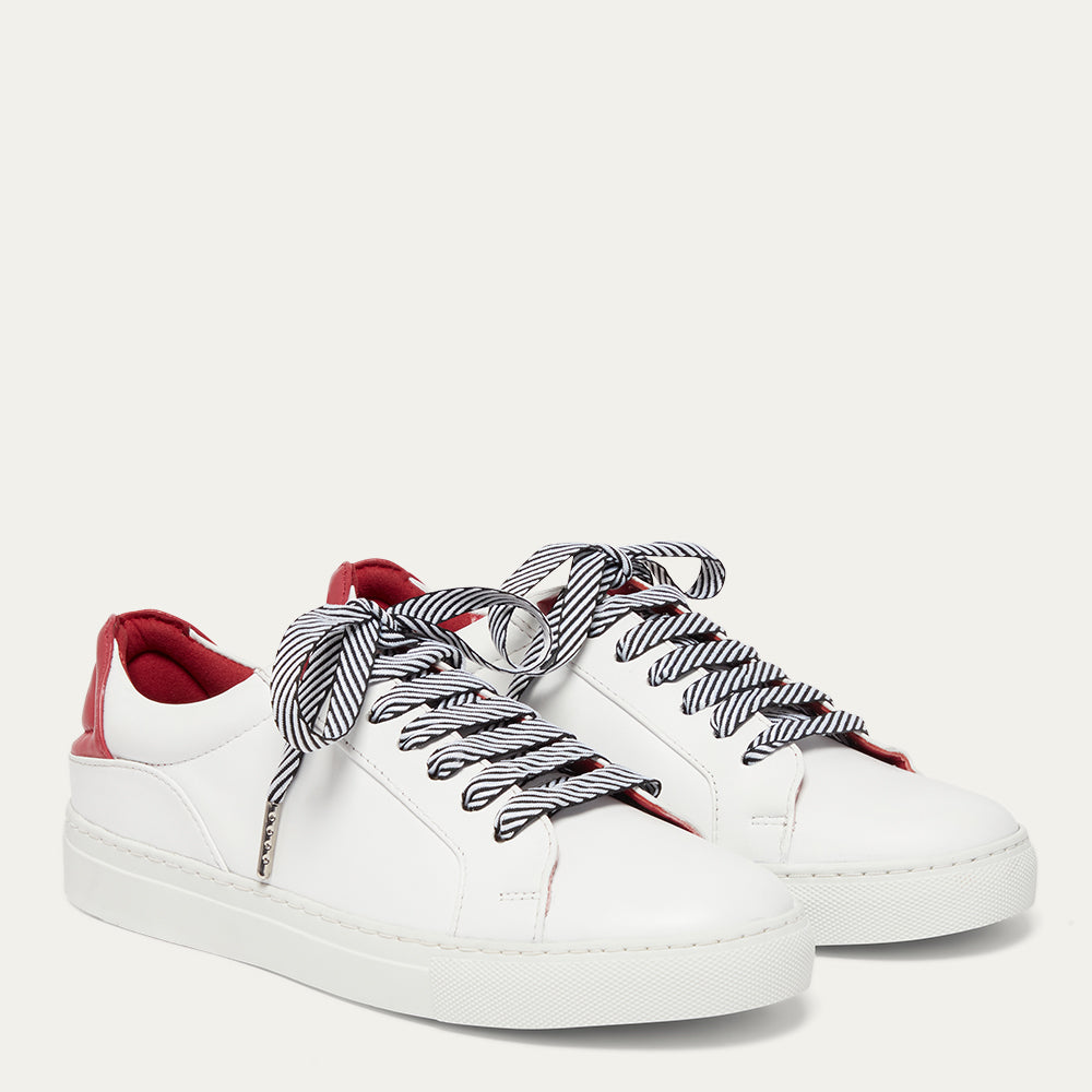 White sneakers with red accents and black and white striped laces on a light gray background