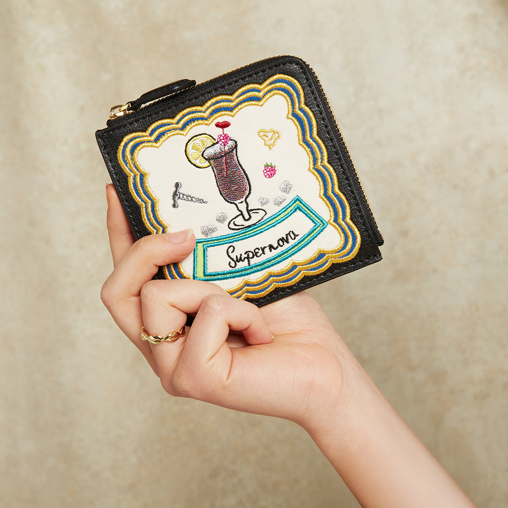 Hand holding a wallet with embroidered design on a beige background